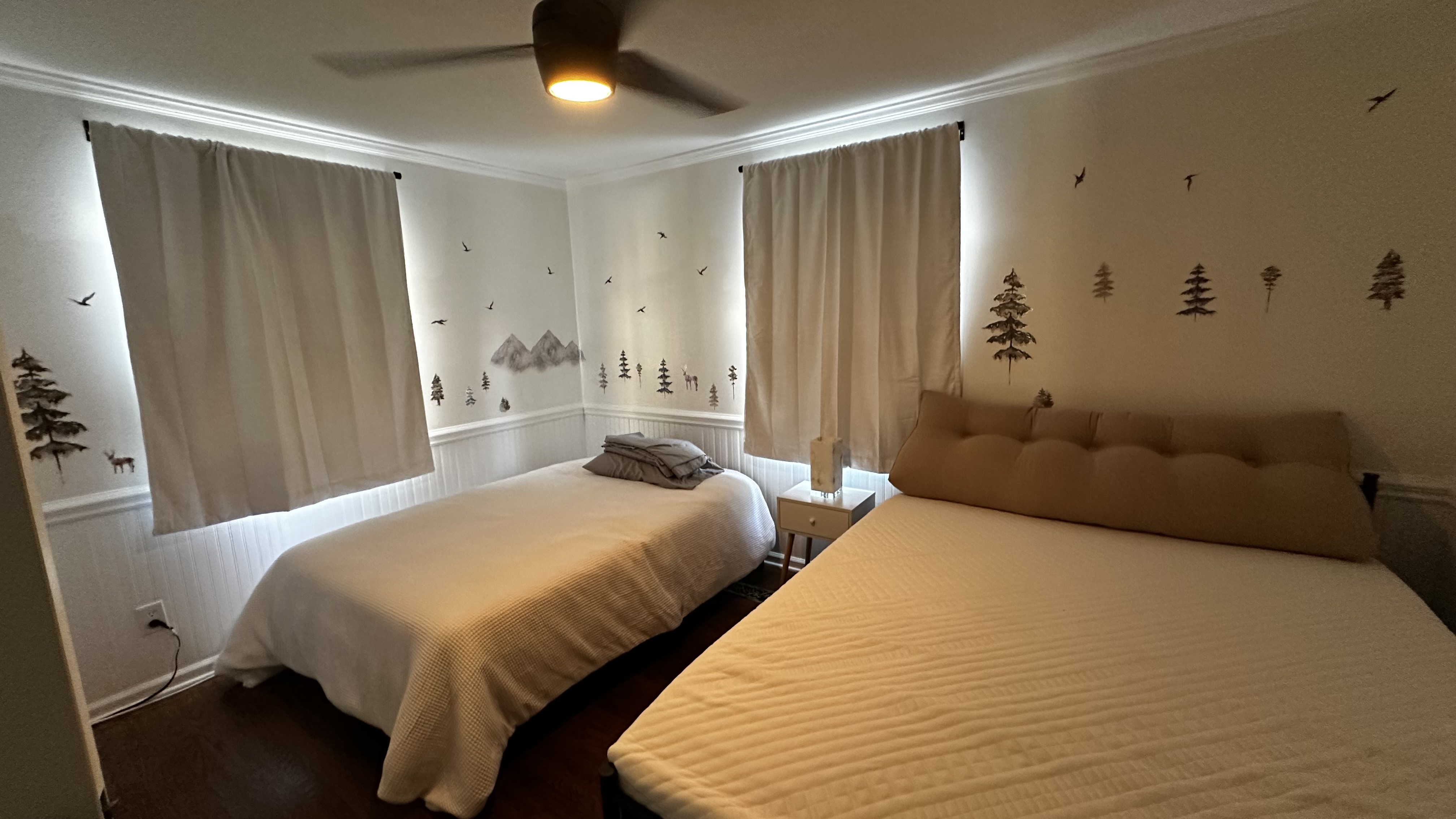 A serene bedroom with a mountain theme, featuring two beds, curtains, and wall decals.