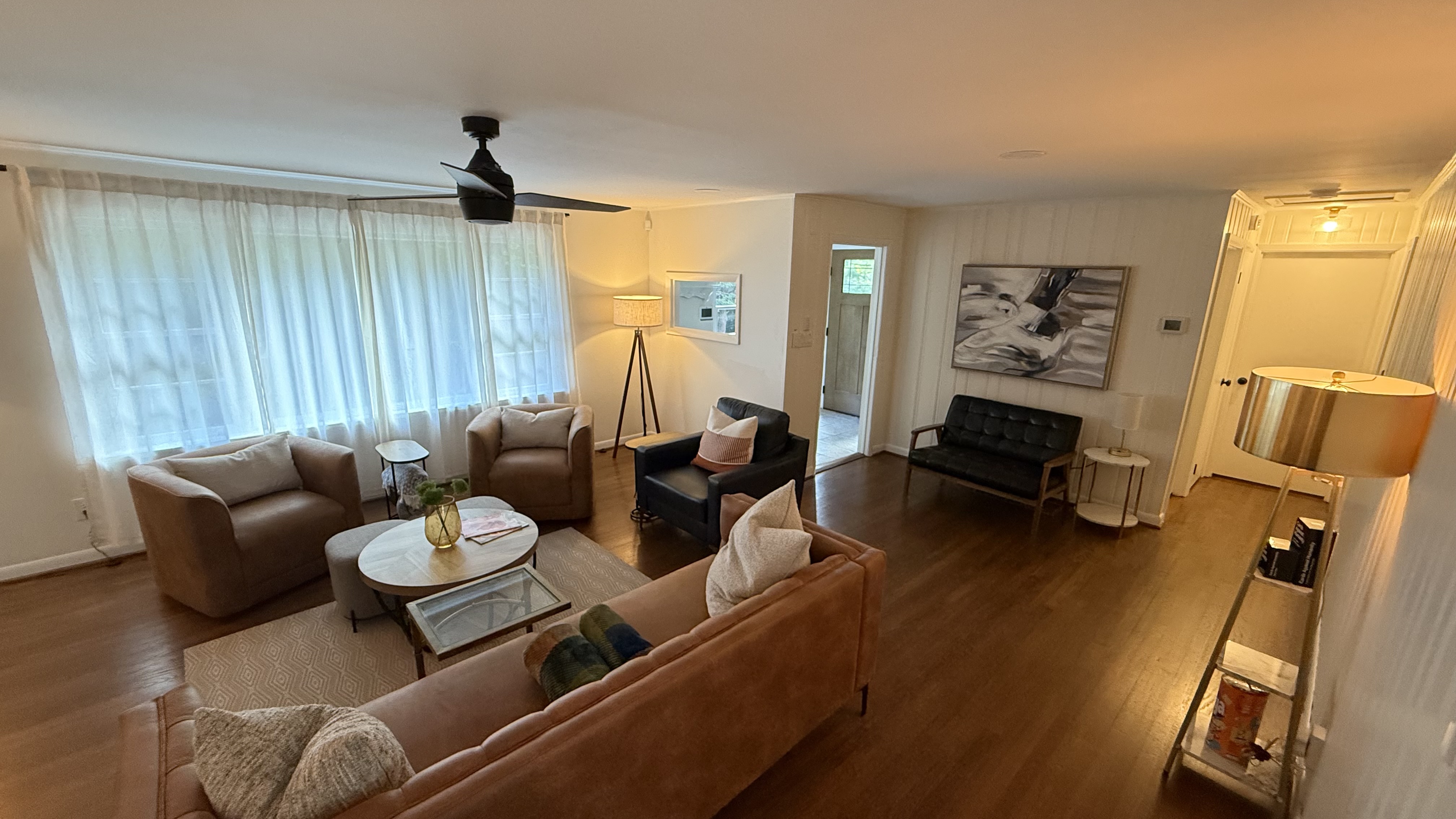 A living room with a brown couch, two armchairs, and white curtains.